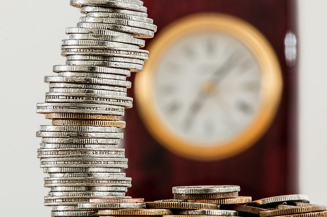 stacked-coins-in-front-of-blurred-clock
